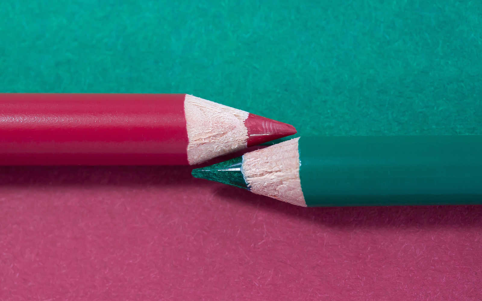 Deux crayons de couleur pourpre et émeraude qui se font face sur une surface divisée dans les deux couleurs